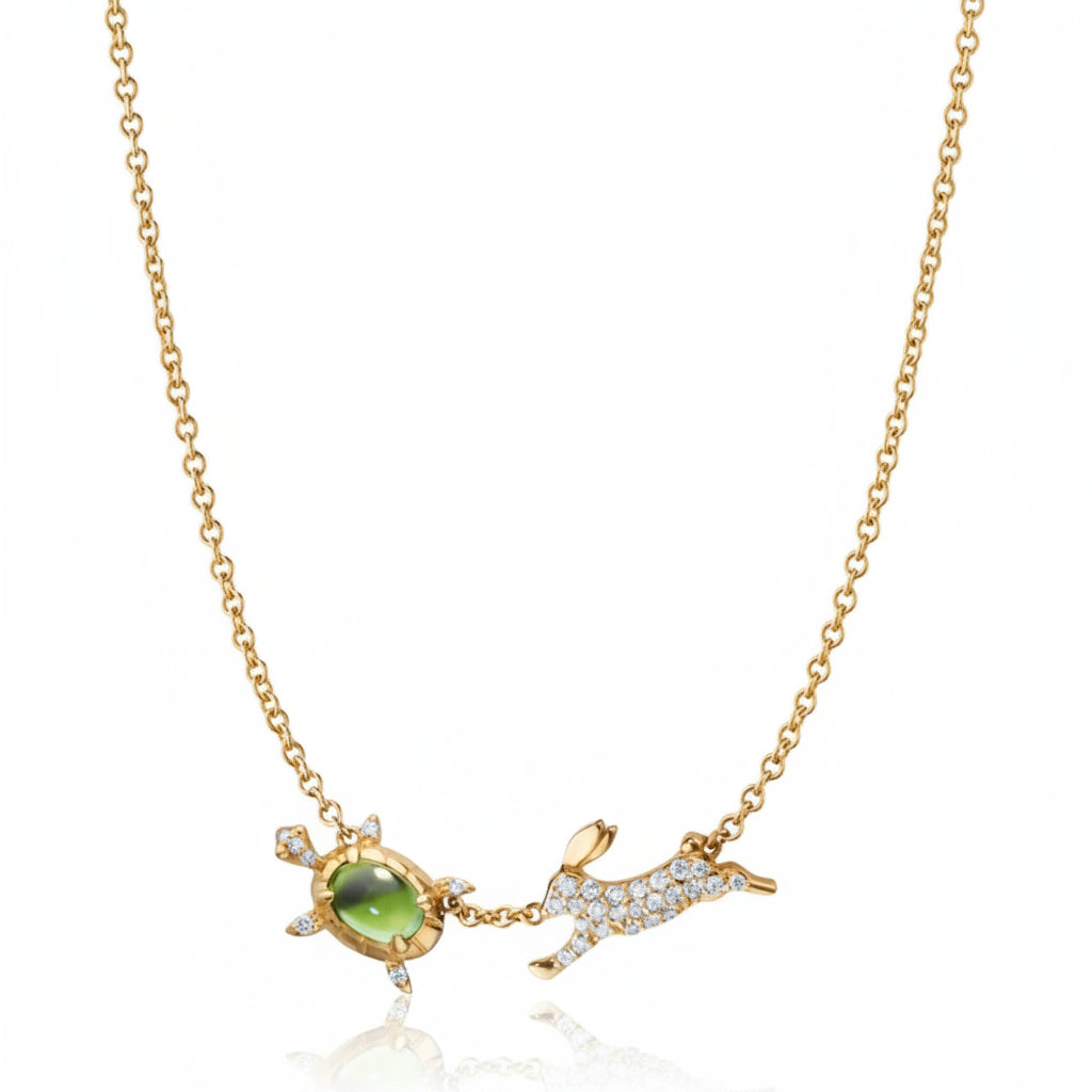 Gold necklace with a green gemstone and a small animal pendant on a white background